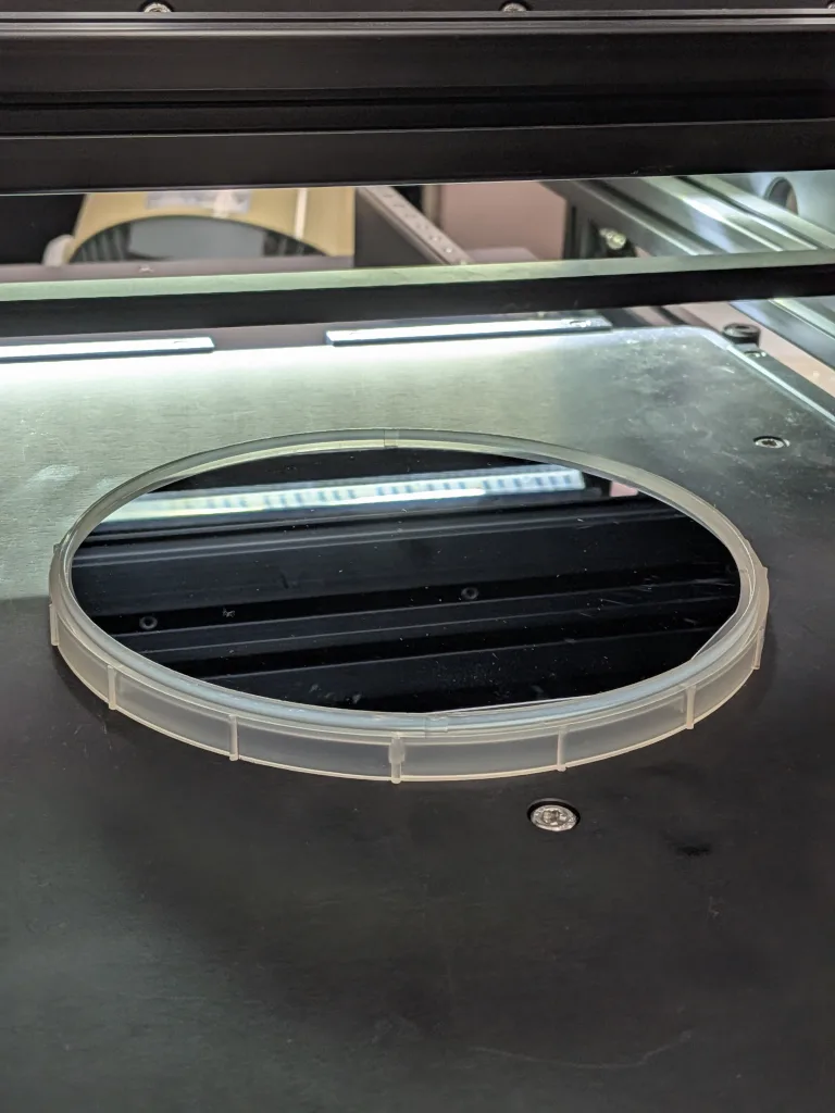 TR-300検査ステージ上のプラスチックリングに載った6インチシリコンウェハ。鏡面にLED照明バーが映り込んでいる様子
