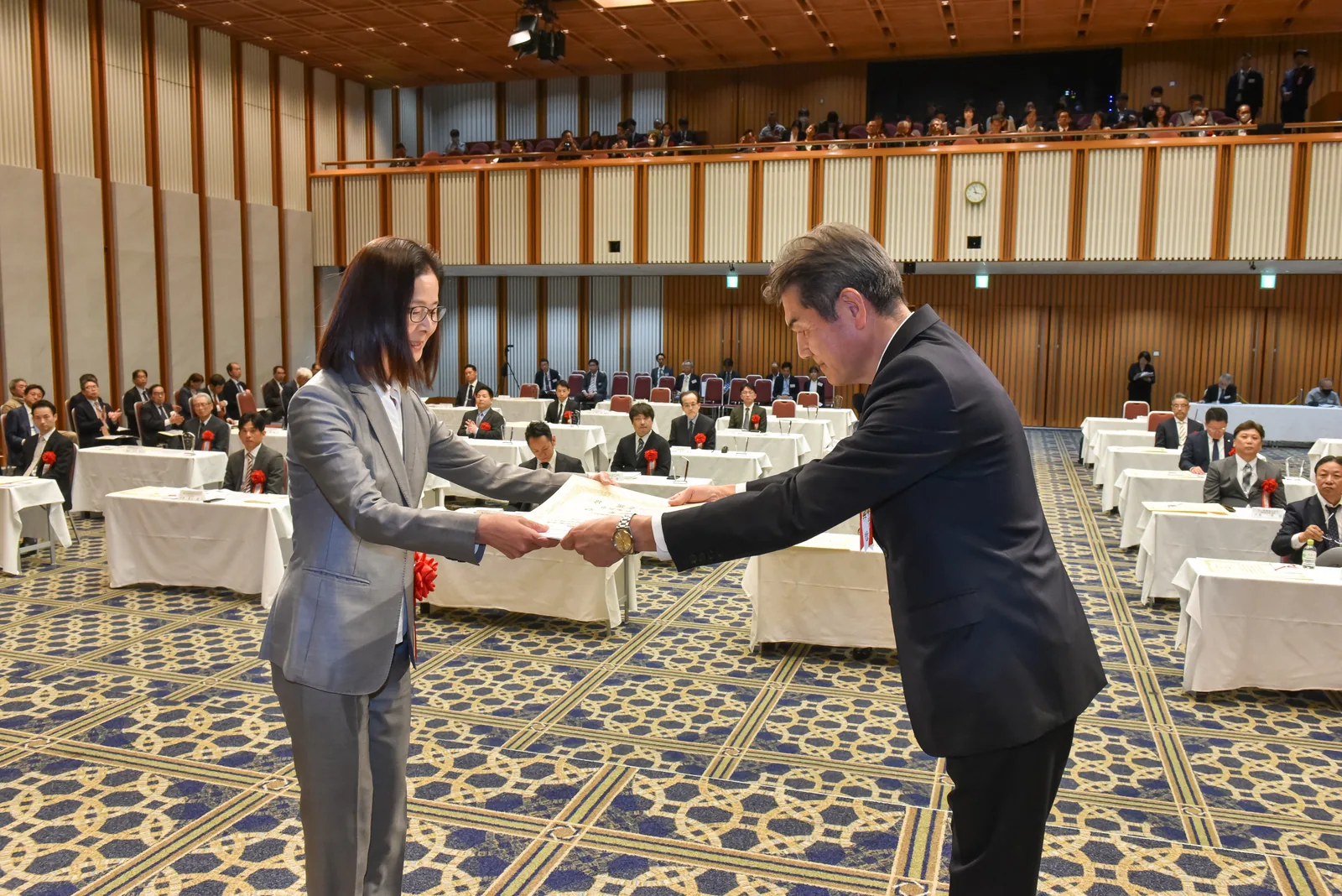 第38回 中小企業優秀新技術・新製品賞 贈賞式の様子。会場の正面で、当社の受賞者に賞状が手渡されている。後方には着席した出席者が並んでいる。