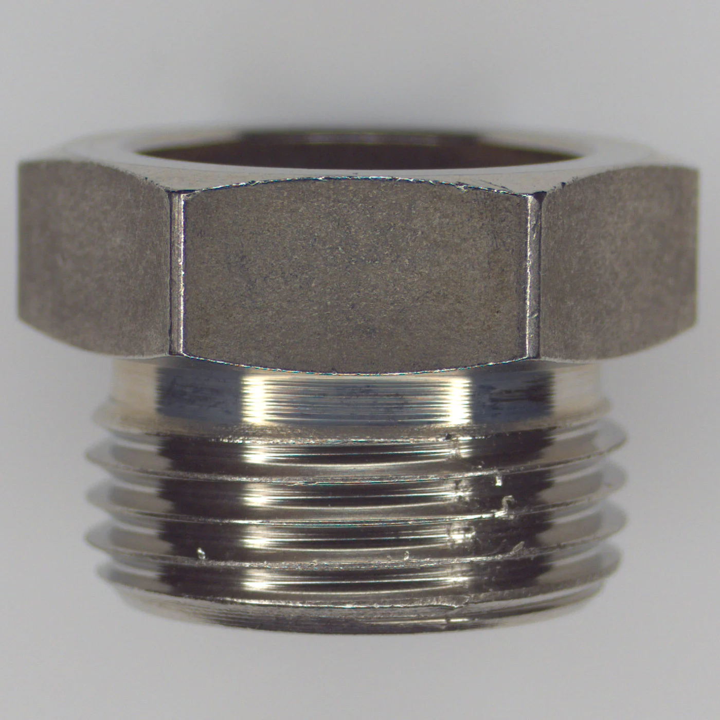 The same stainless steel fitting photographed with an ordinary camera. Reflection from the metal runs along the thread and the dent is lost in the streak of light.