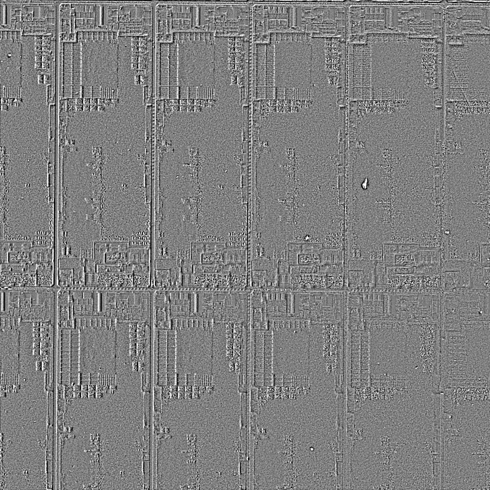 3D Surface output of the same semiconductor chip. The interference colours are gone entirely; the steps between circuit blocks, the grooves of the scribe lines dividing the dies and the relief of the fine wiring pattern stand up like a plaster cast. Towards the right of the frame a particle resting on the surface appears as a bright grain.
