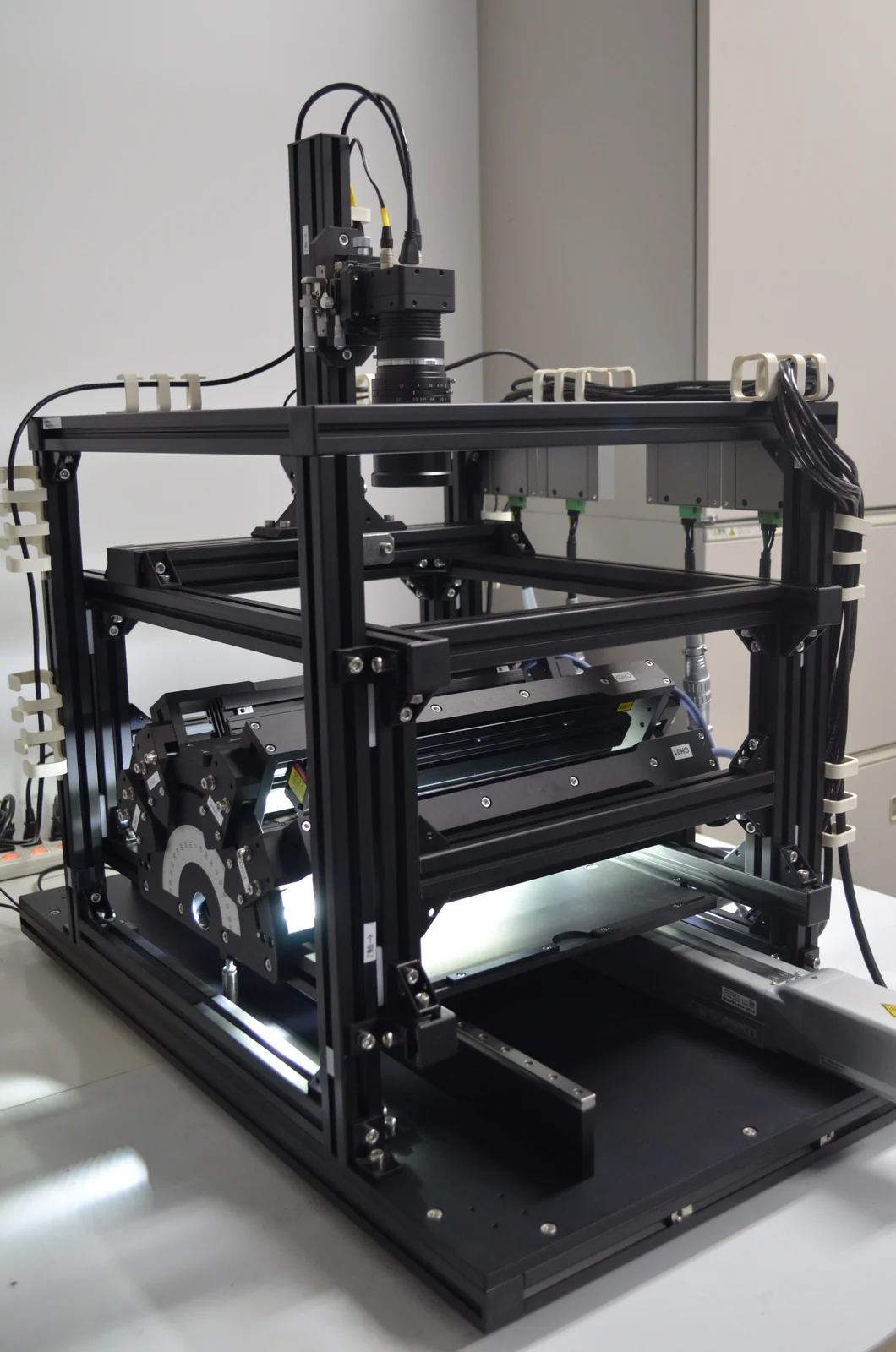 3D × AI 外観検査システム TR-300 の外観。黒いアルミフレームで組まれた筐体の上部にカメラ、内部に多方向の照明ユニットが配置されている。