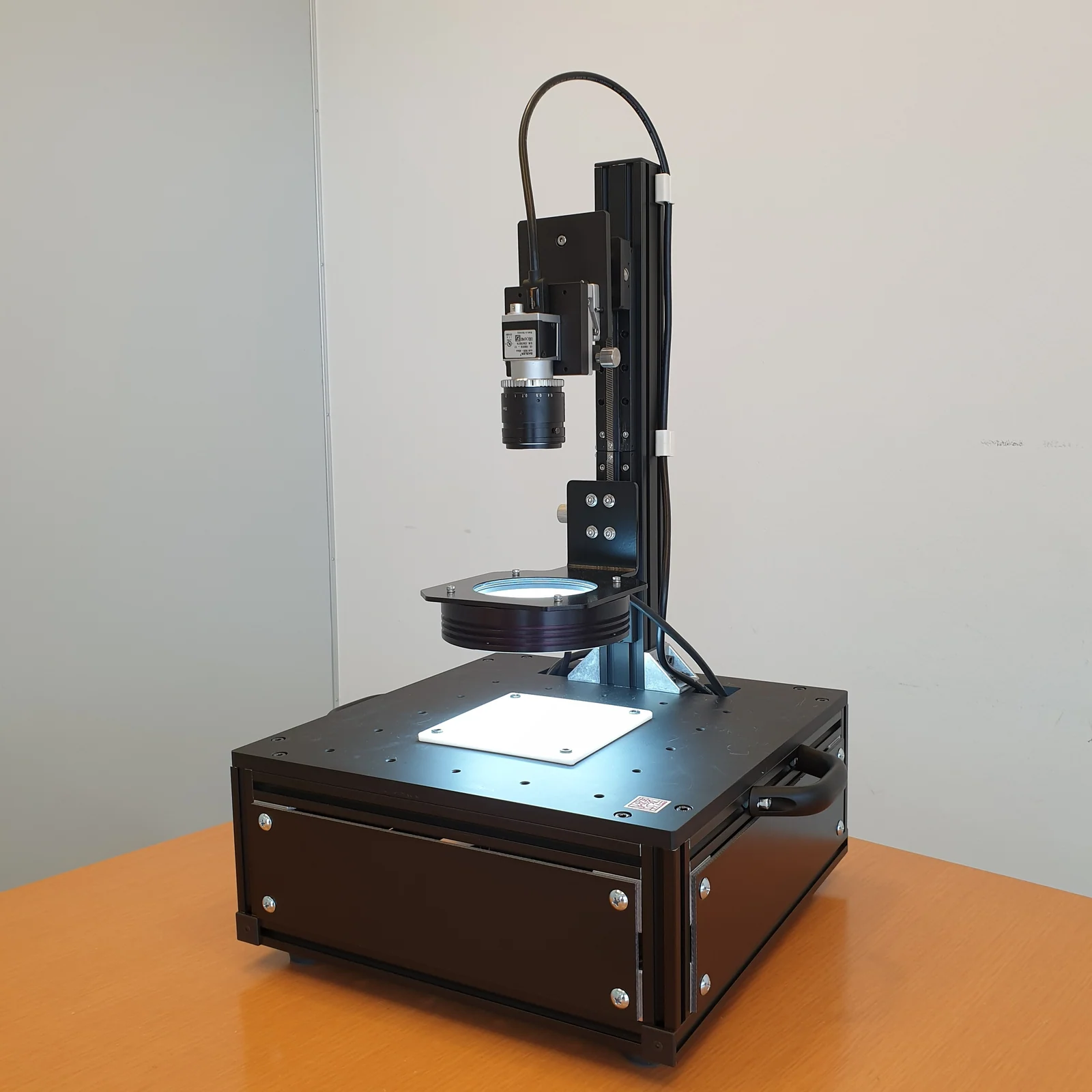 表面 3D 観察装置 TR-55 の外観。卓上に置けるサイズの筐体と、円形の照明ユニットを支える縦のアーム。